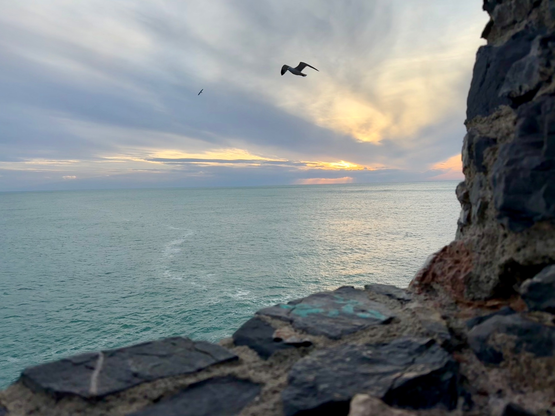 Sunset over the open sea seen from the old stone ramparts, light breaking through the clouds